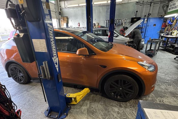 Inside a service bay at Zack's Auto Service, with a car raised on the lift and a technician working on a second car behind it.